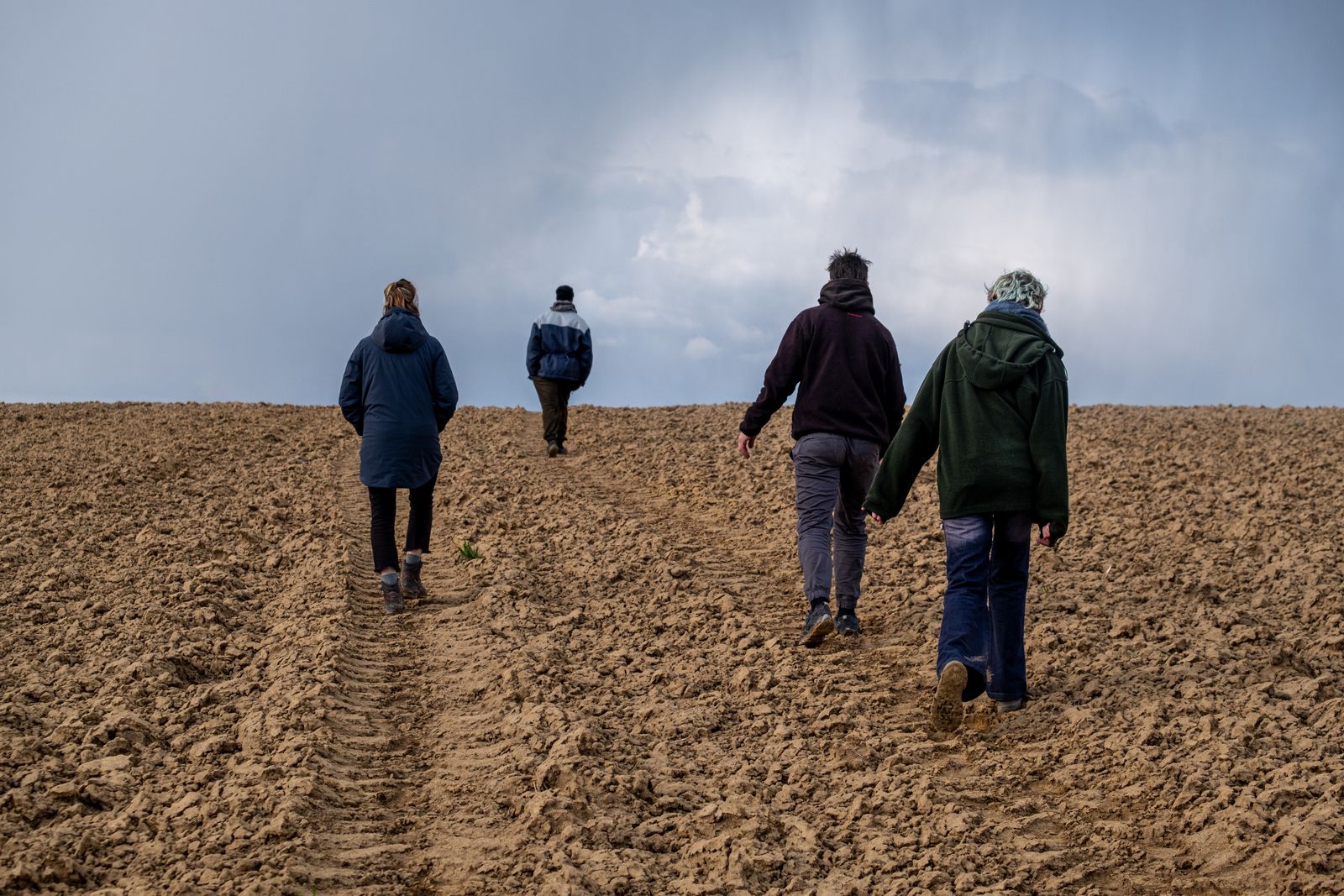 Four people in warm coats walking across a ploughed field, seen from behind