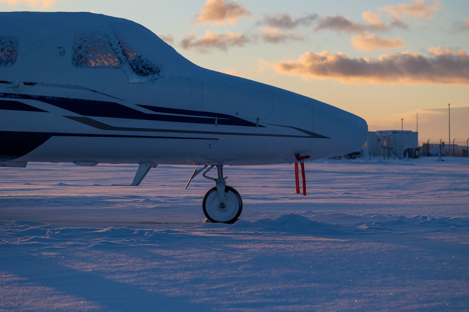 Nose of a business jet dusted with snow on a winter airfield at sunset