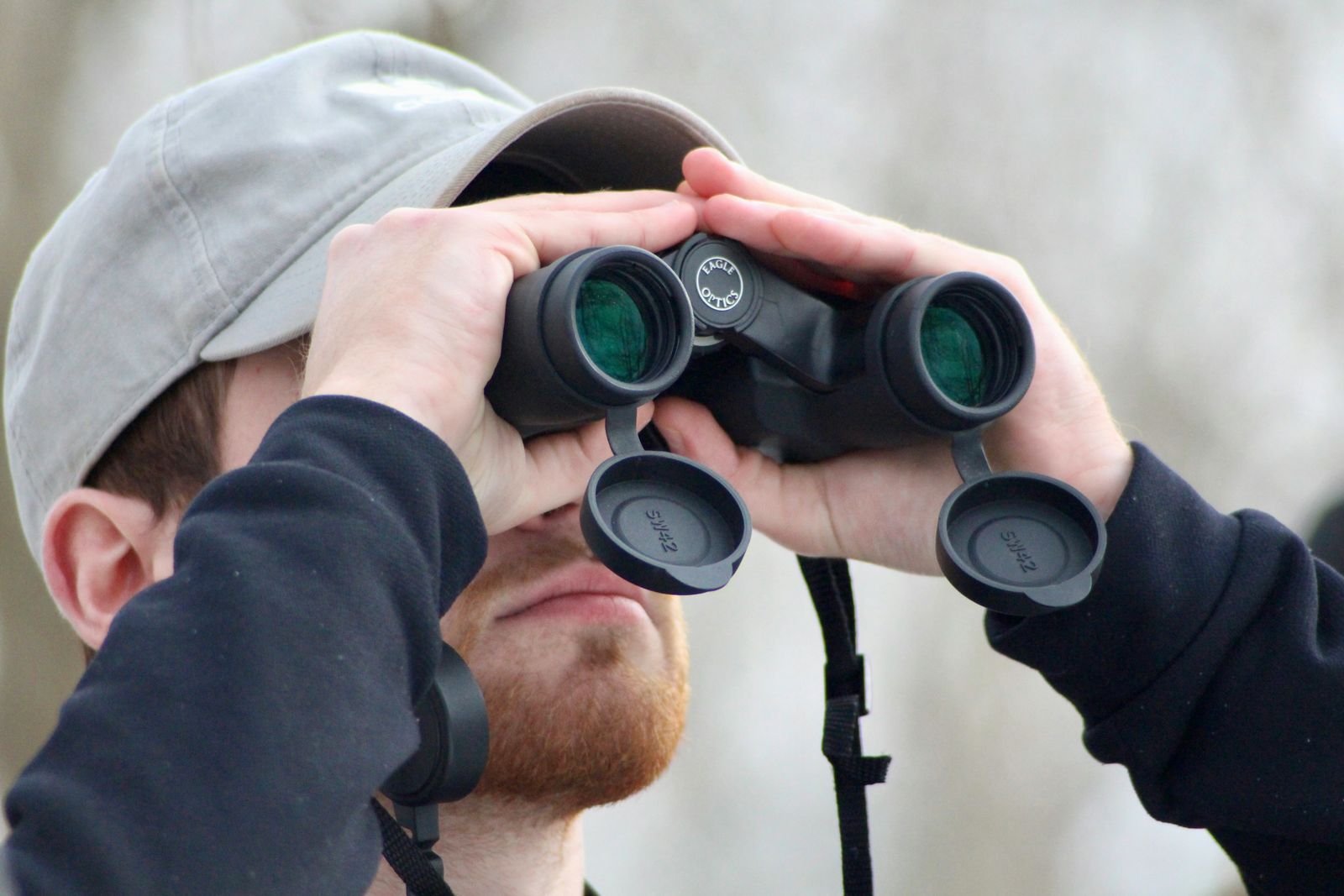 A man in a grey cap looking up through binoculars