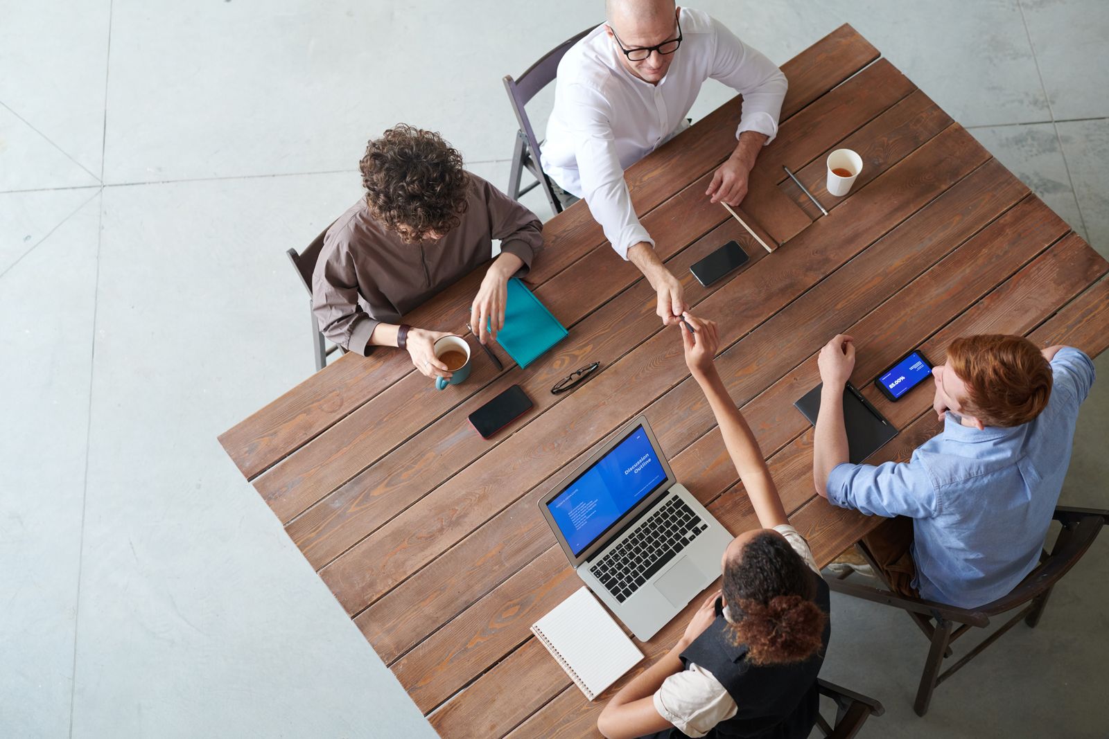 A small team around a wooden table with laptops, tablets and coffee, seen from above