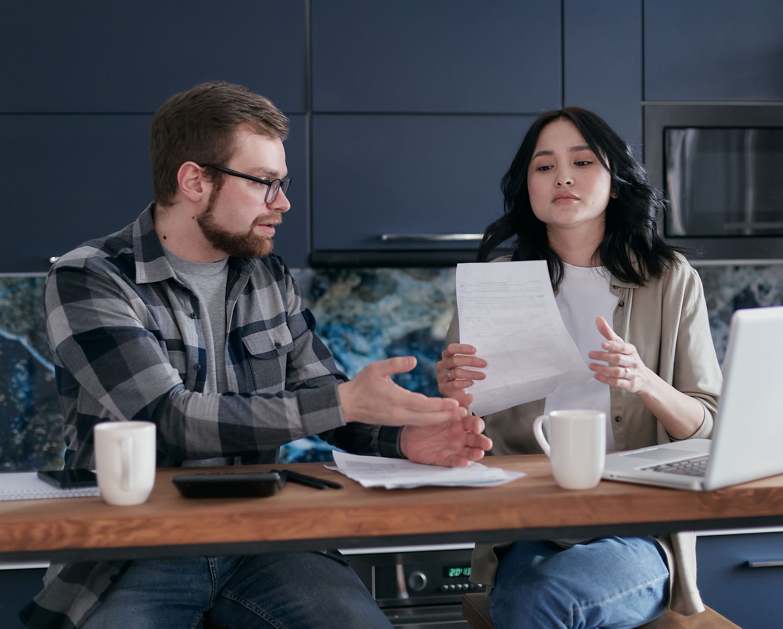 A couple at a kitchen table going through letters and bills with a laptop open