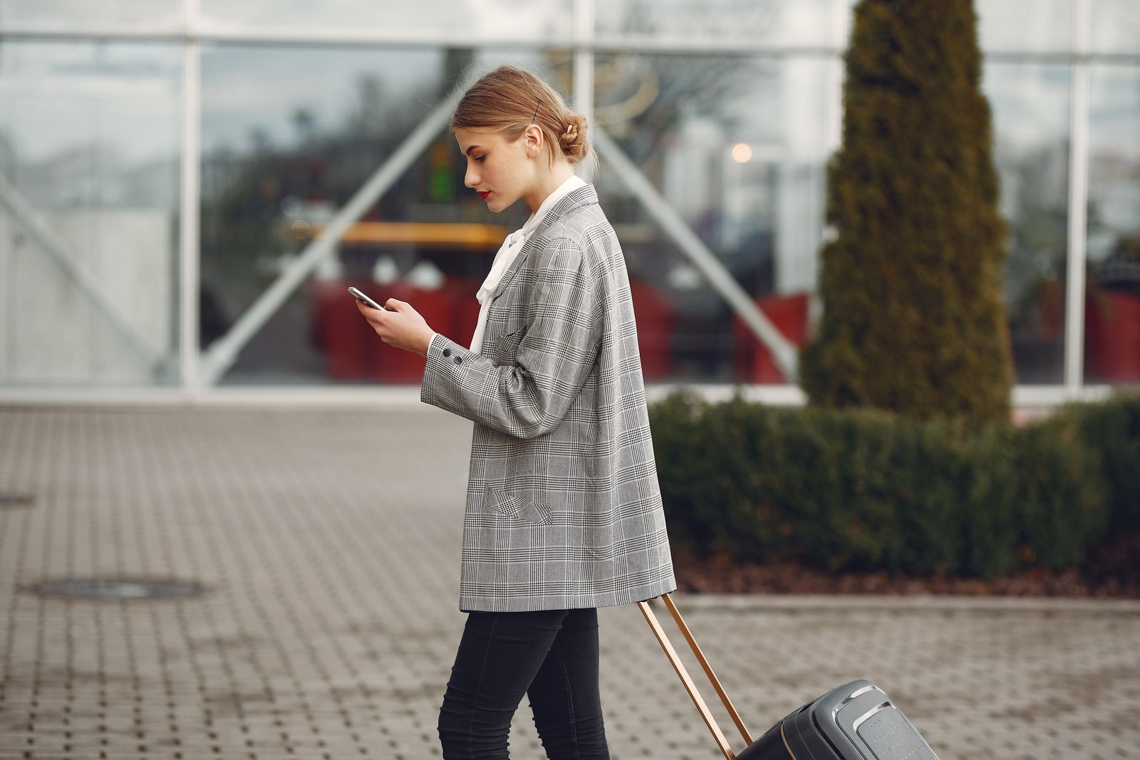 A woman walking with a suitcase outside a station, looking at her phone