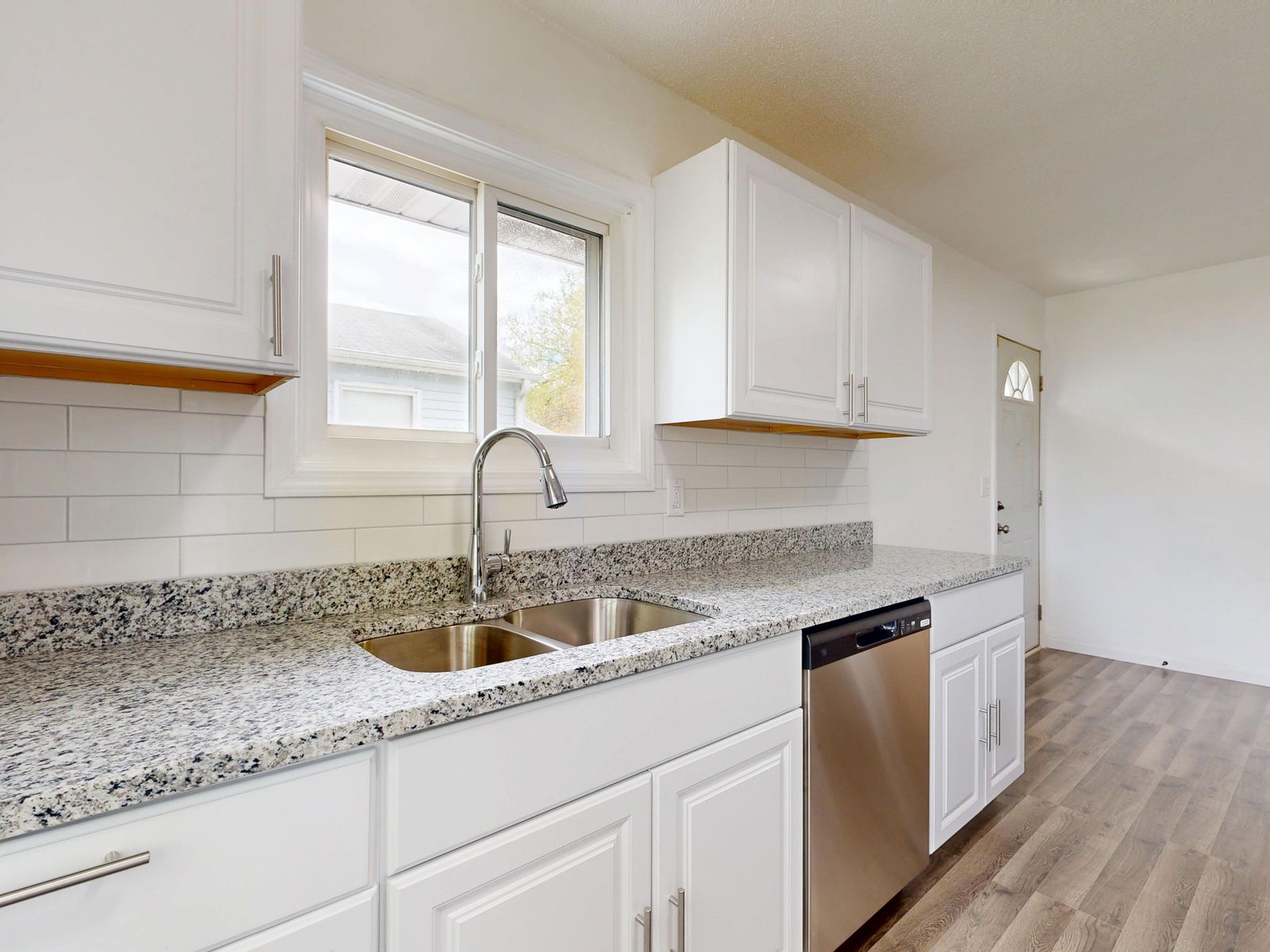 Bright new kitchen with white cupboards, a speckled worktop and a window over the sink