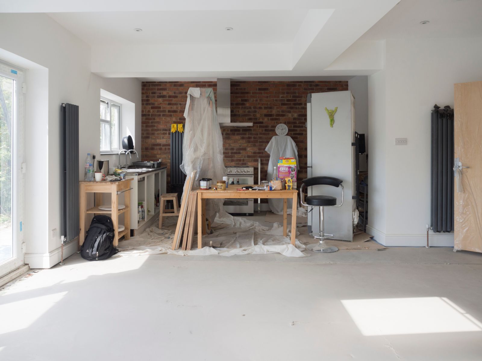 Open-plan room at fixing stage with plastered walls, a radiator and tools on the floor