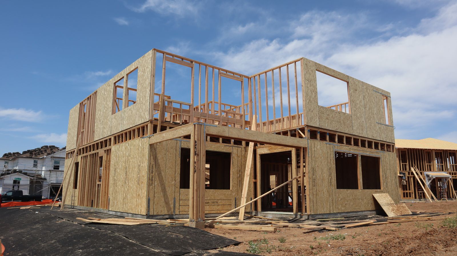 Two-storey timber frame of a new house with sheathed walls under a blue sky