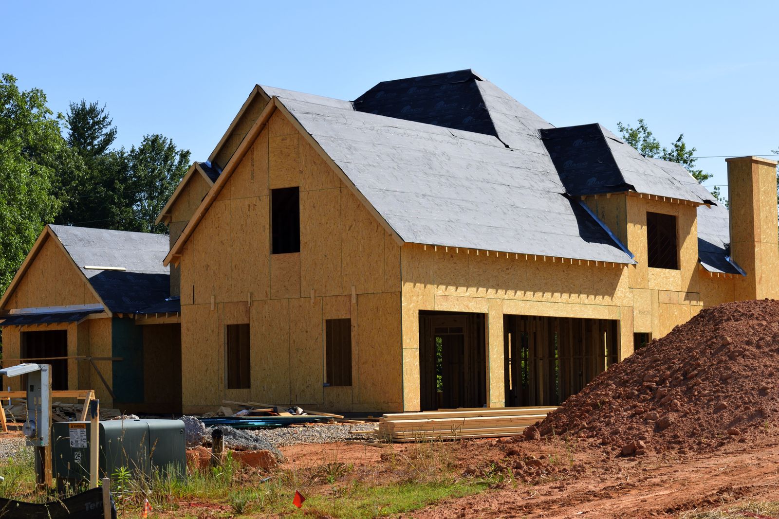 Timber-framed house at lock-up stage with roof sheathing on and window openings cut