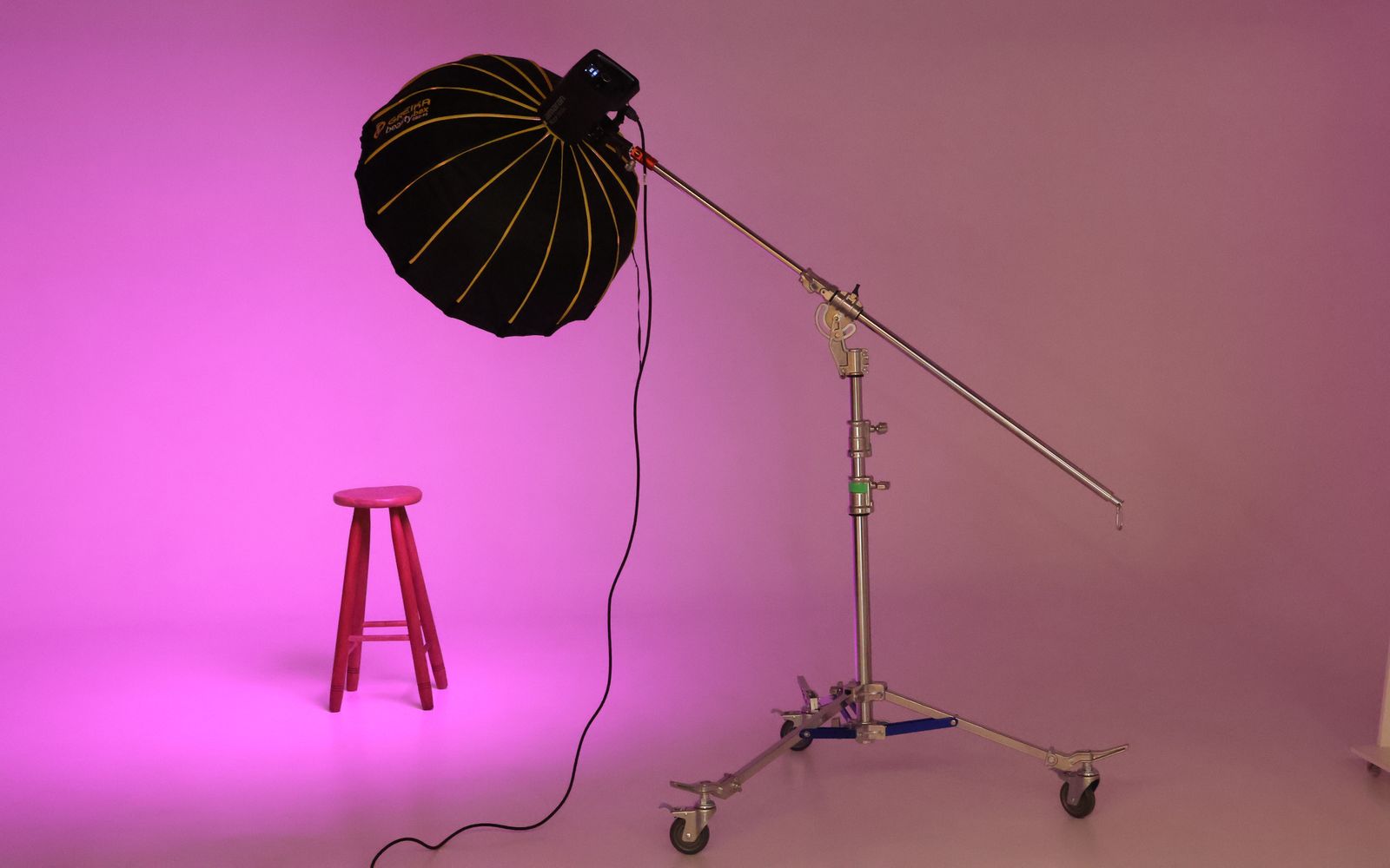 Stool on a pink paper backdrop lit by a large umbrella on a boom stand