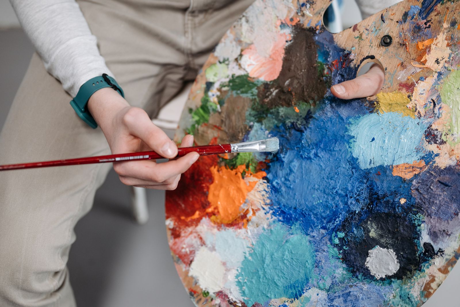 A hand mixing oil colours on a wooden palette with a brush