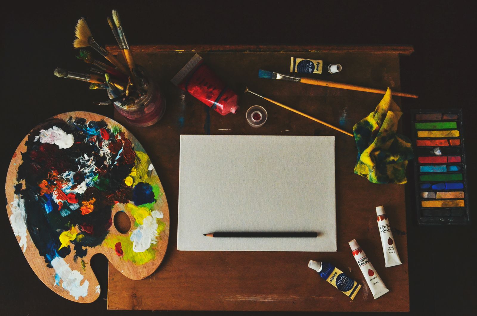 Brushes, paint tubes, a palette and a blank canvas on a work table