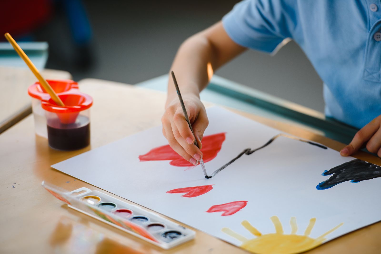 A child's hand painting with watercolours at a table