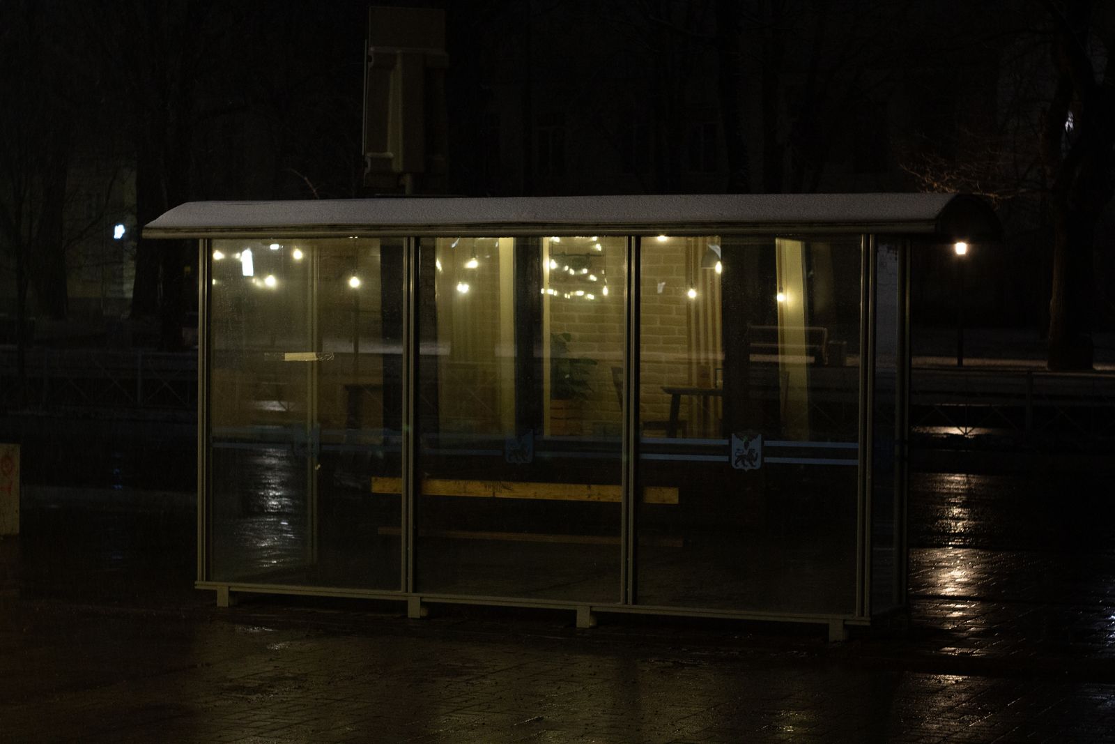 An empty glass bus shelter lit up at night on a wet street