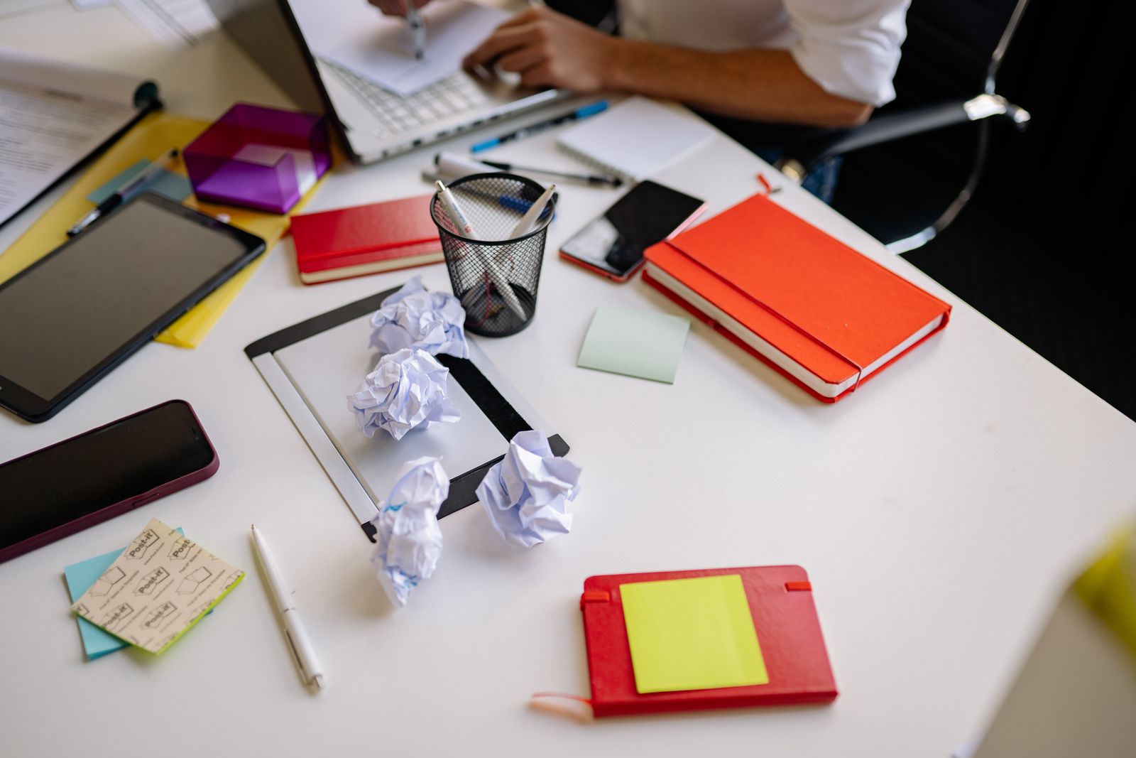 A work desk covered in notebooks, crumpled drafts and stationery