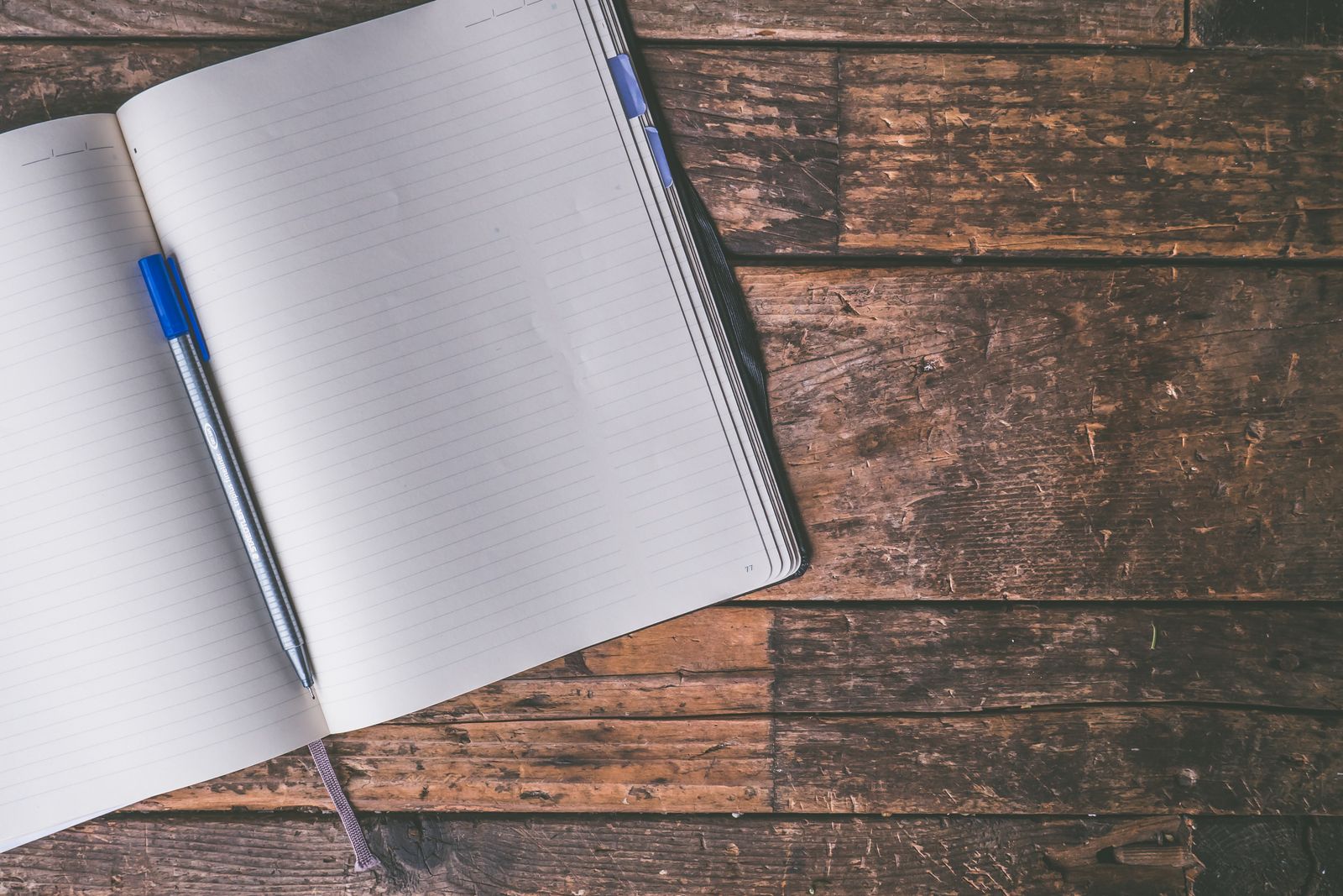 An open notebook with a blue pen on a wooden table
