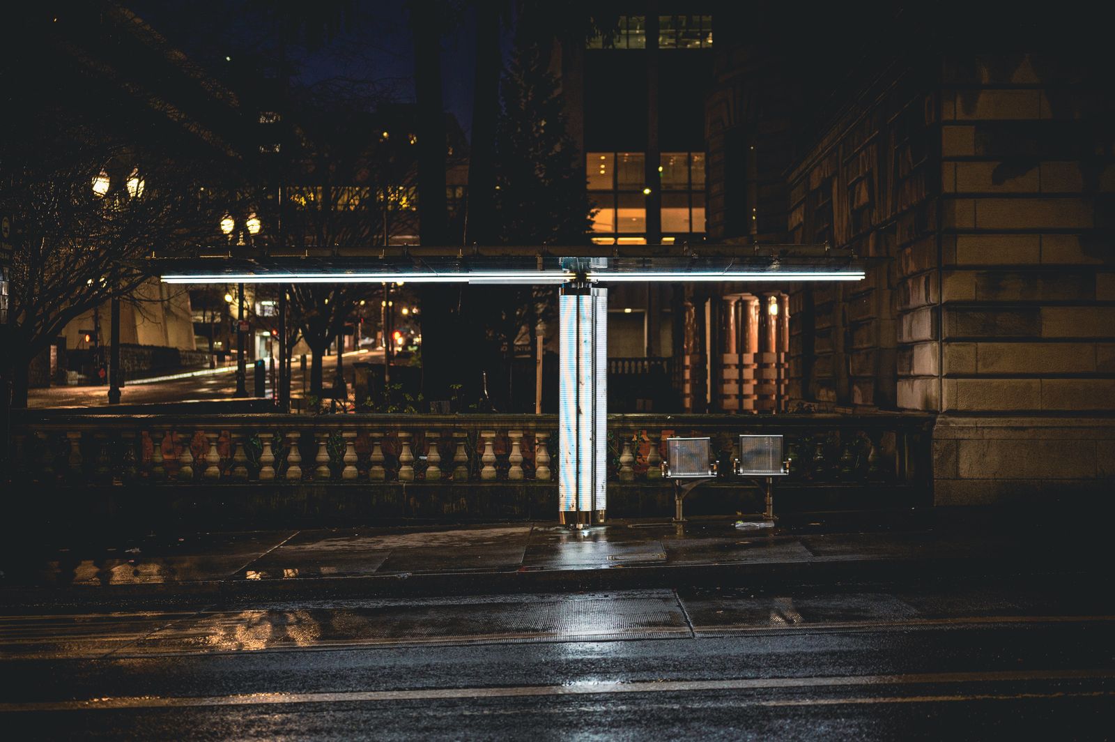 A lone bus stop lit by street lights on an empty street at night