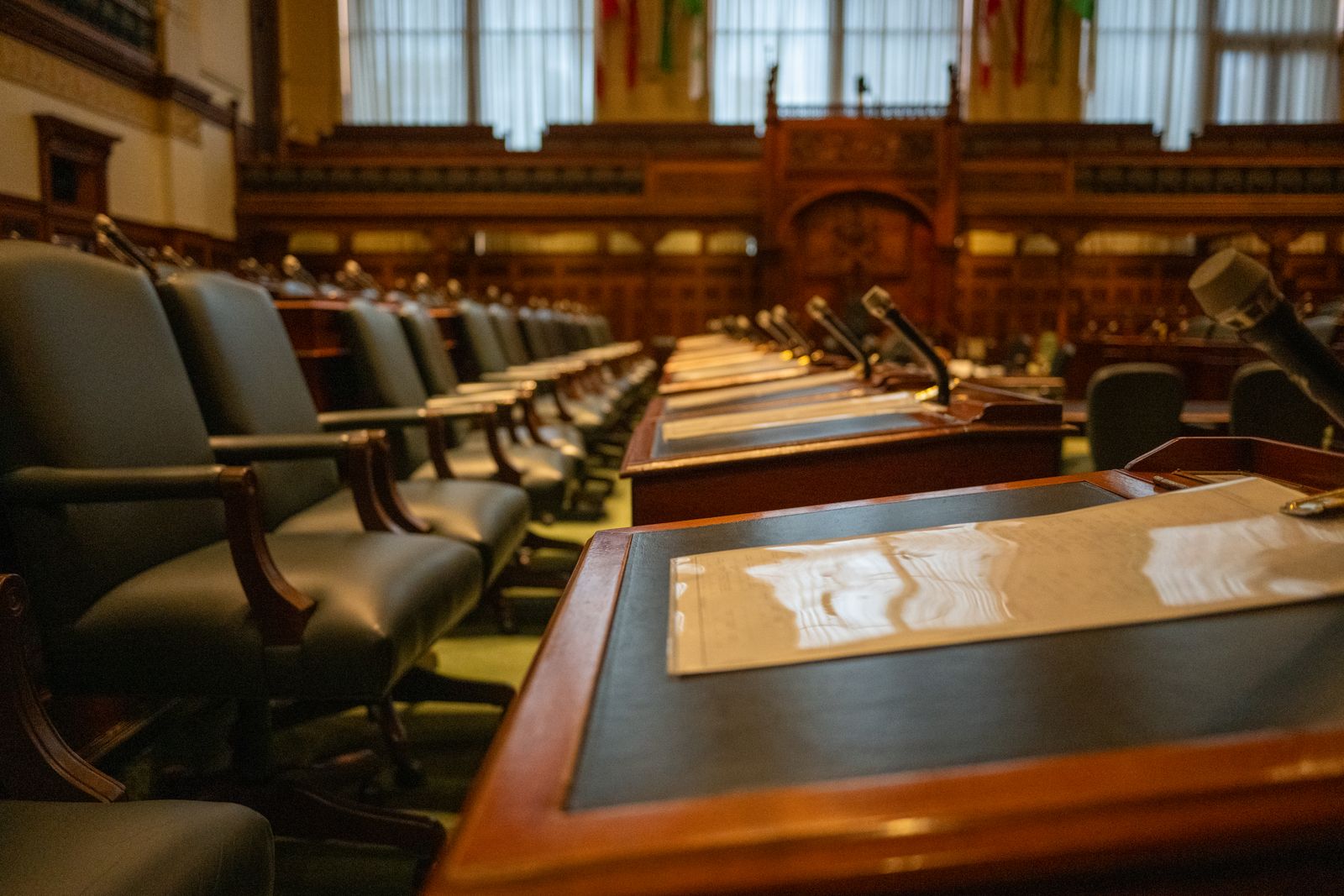 An empty council chamber with wooden desks and microphones