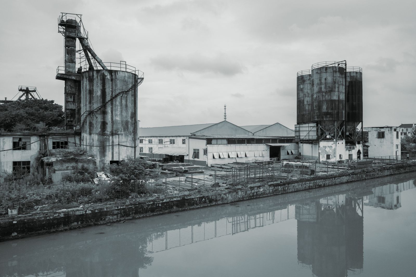 Black and white view of rusting silos beside a river