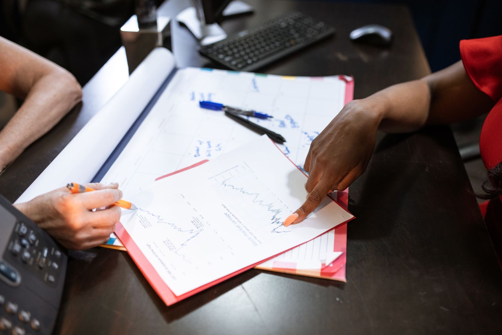 Two people going through printed graphs on a desk, one taking notes