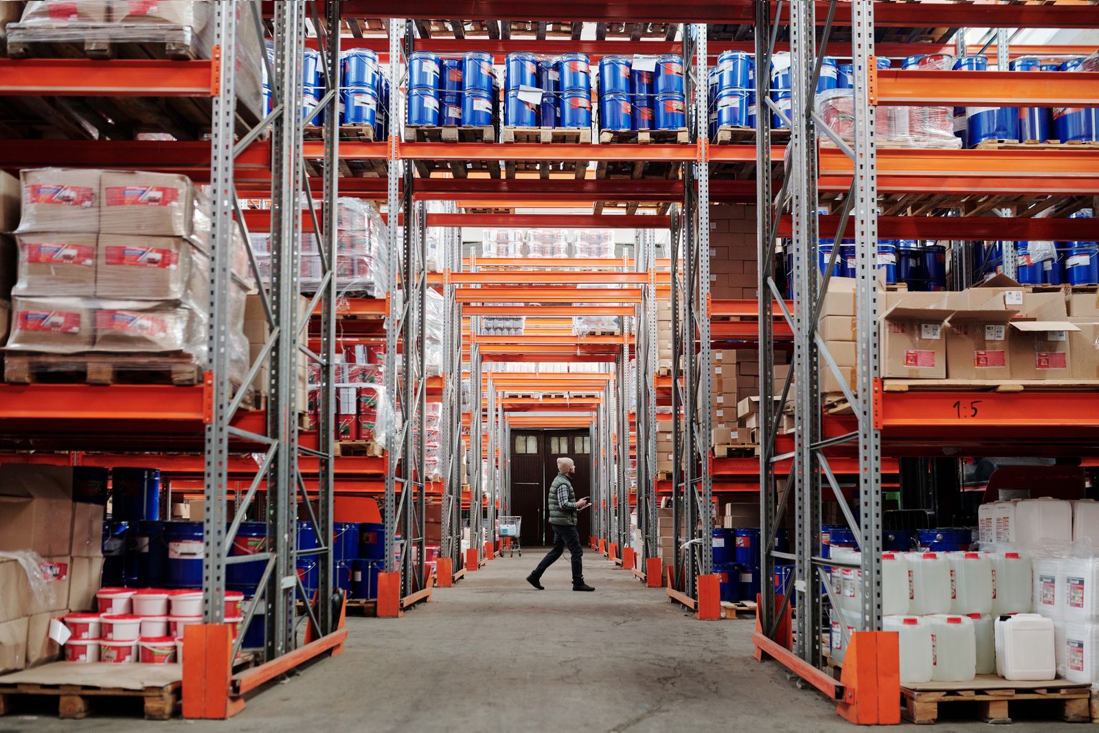 A man walking down a long warehouse aisle between tall stacked shelves