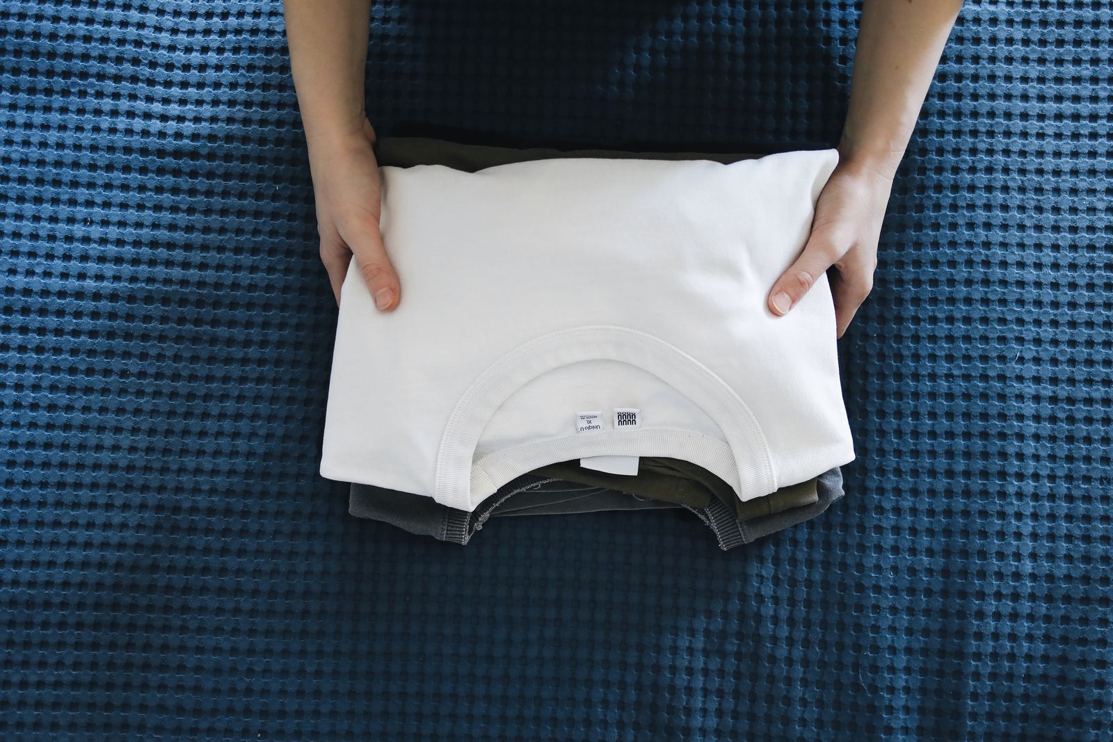 Hands folding a white cotton top on a blue bedspread