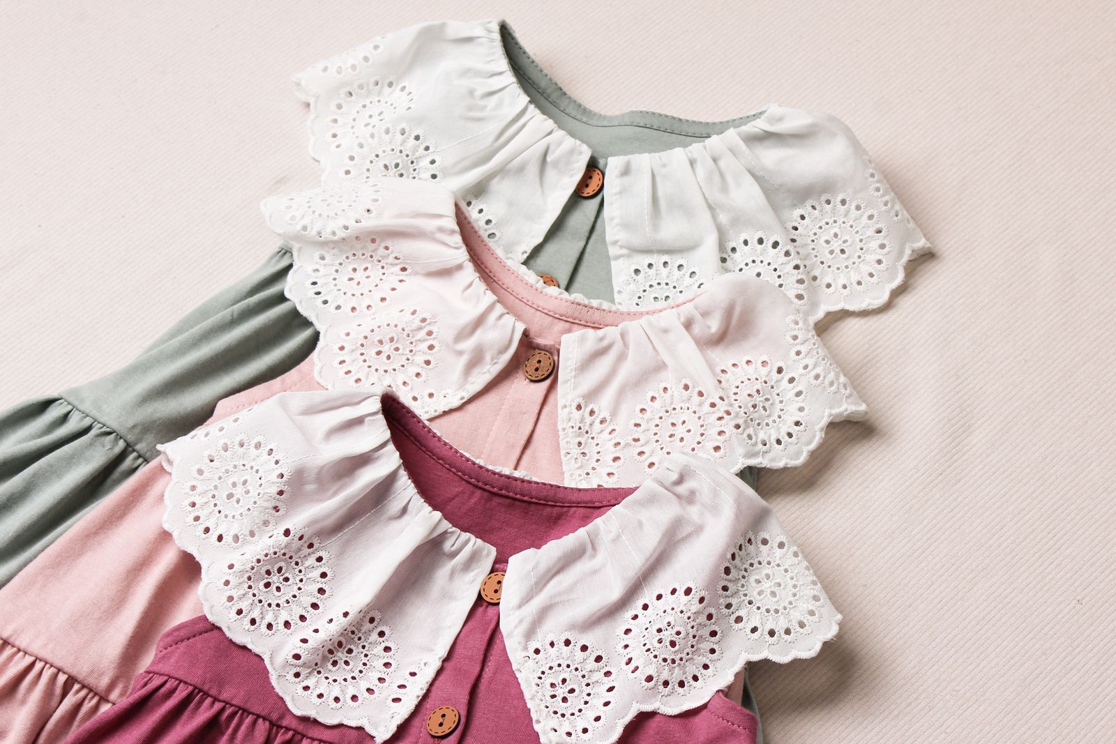 Three baby dresses with lace collars laid side by side