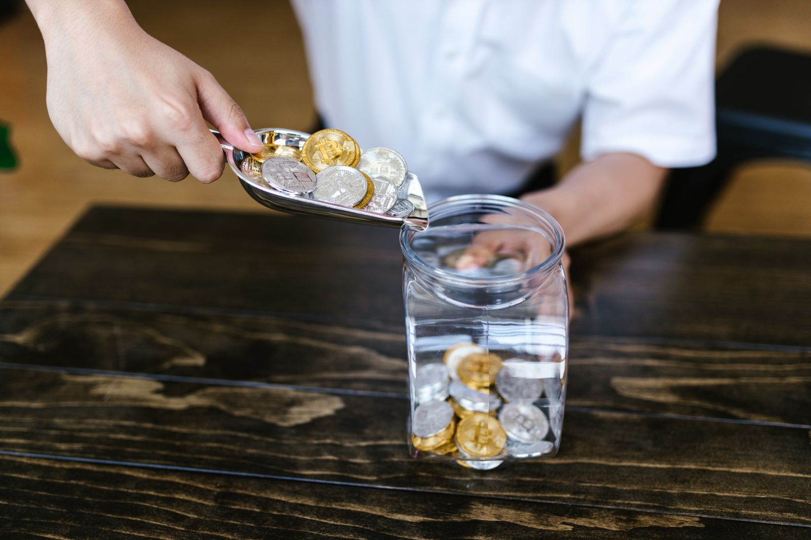 A hand dropping coins into a glass jar on a wooden table