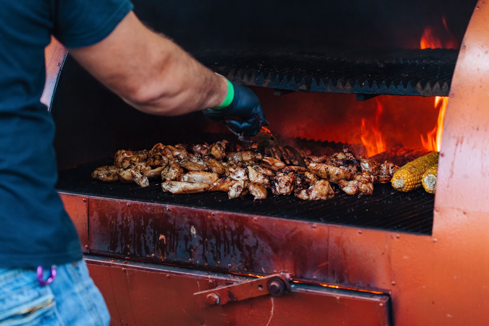 A cook in an apron tending meat on a pit over glowing coals
