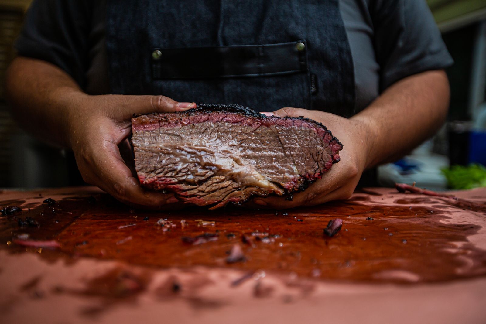 Hands holding a cooked brisket over a wooden board