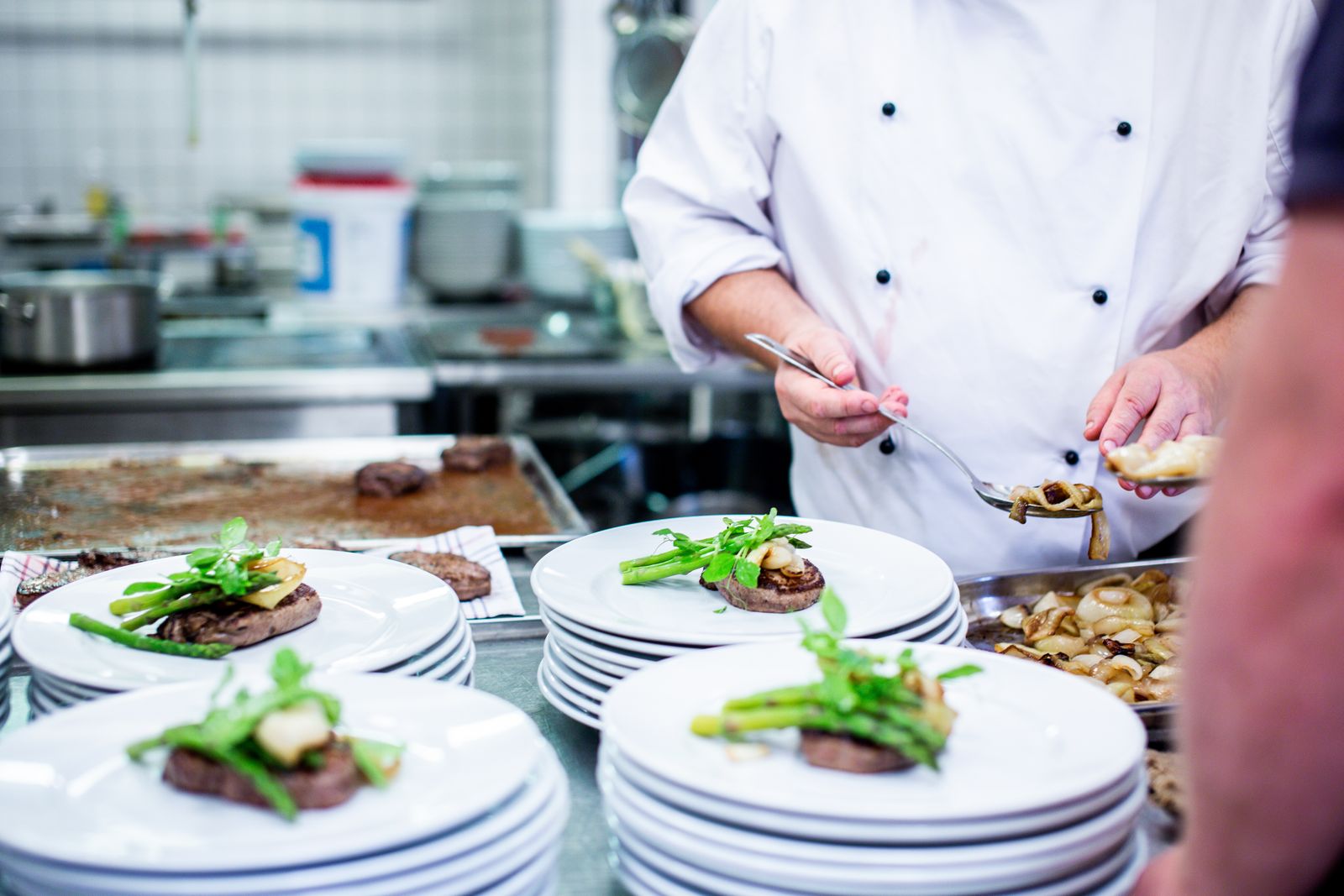A chef finishing plates of food at the pass in a busy kitchen