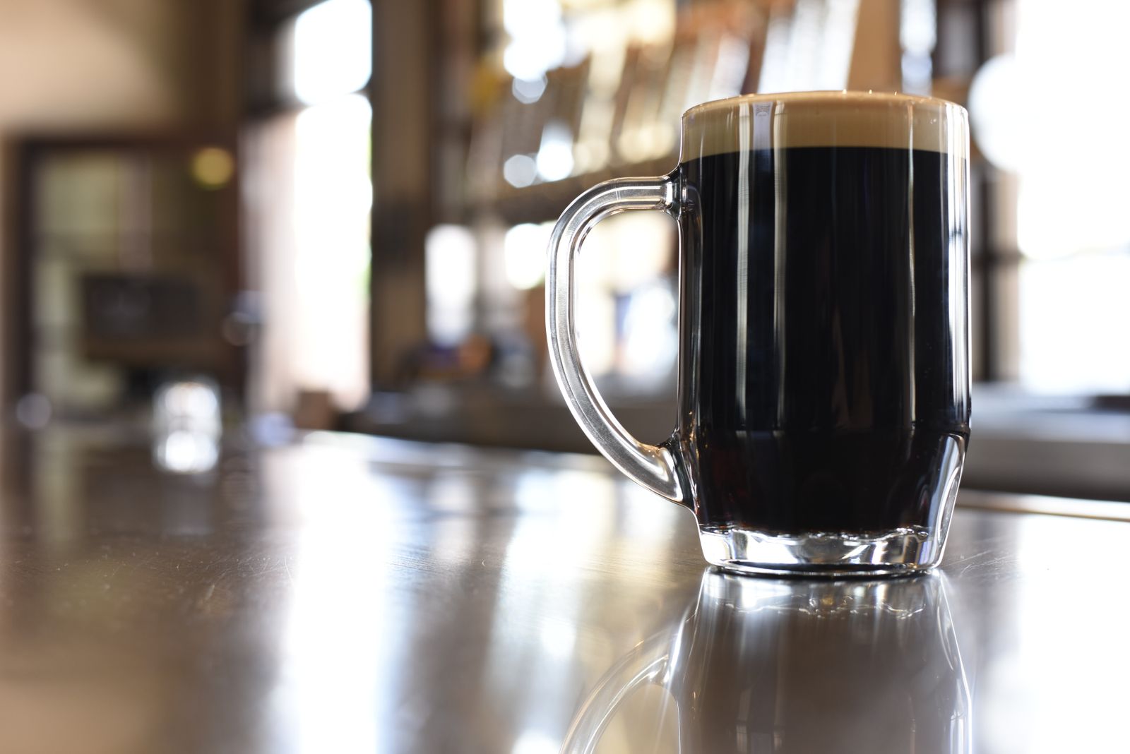 A glass of dark beer with a creamy head on a bar counter