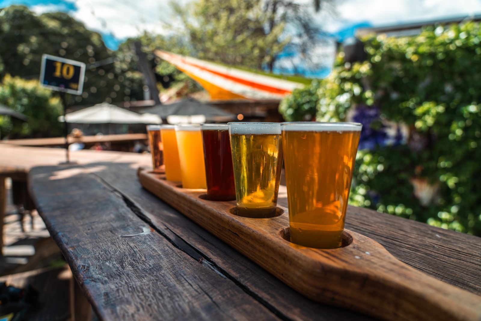 A flight of four beers from pale to dark on a wooden board outdoors