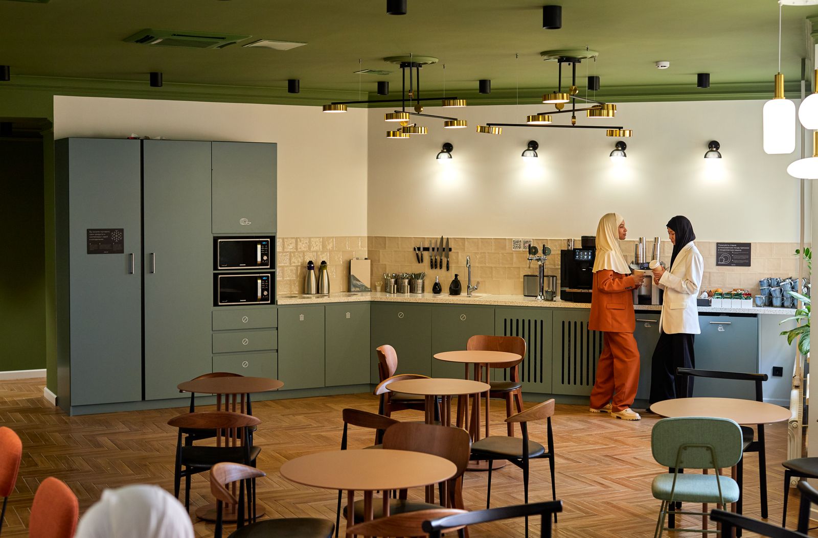 Two members talking at the counter of a shared kitchen with round tables
