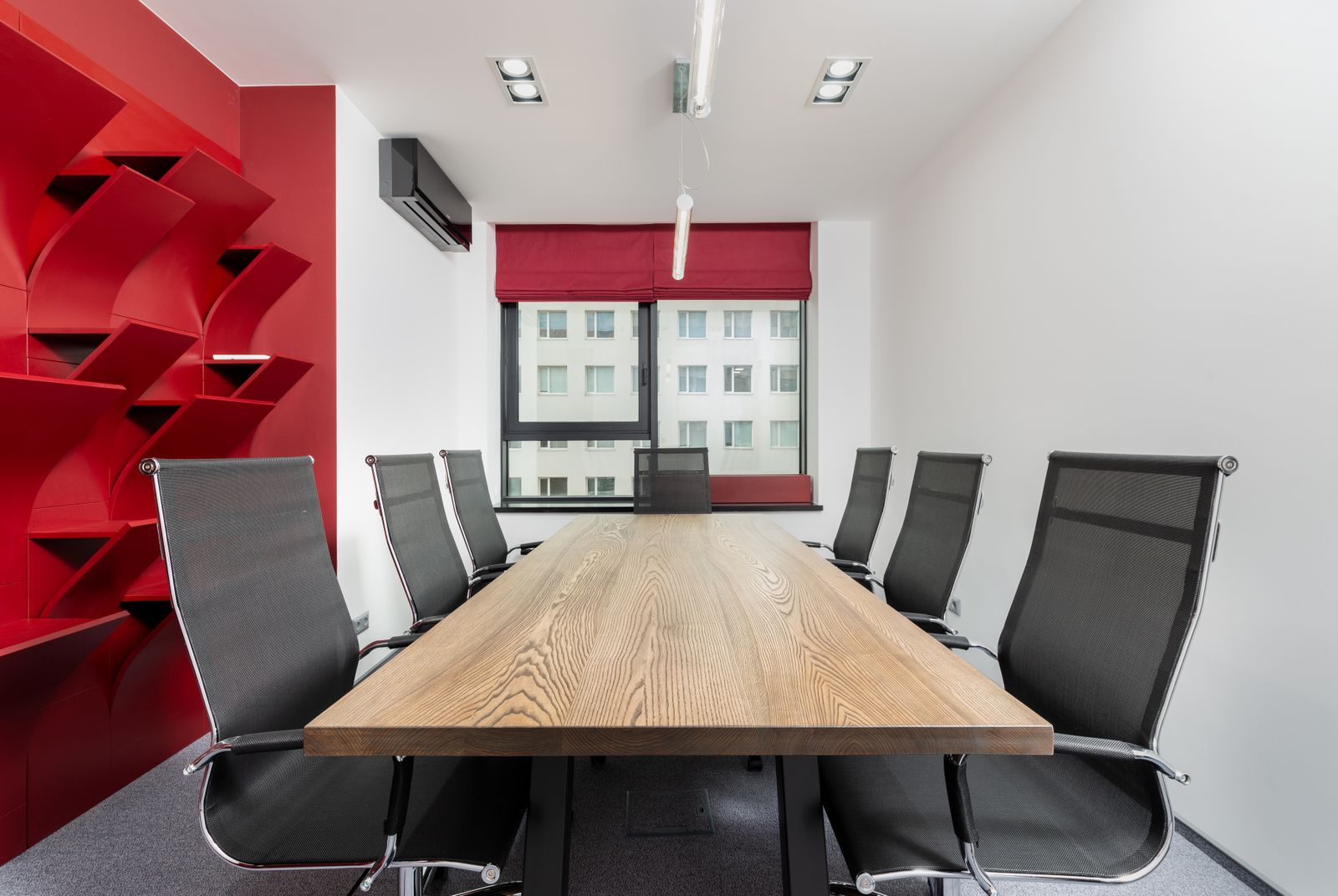 A meeting room with a long wooden table, black chairs and a window with blinds