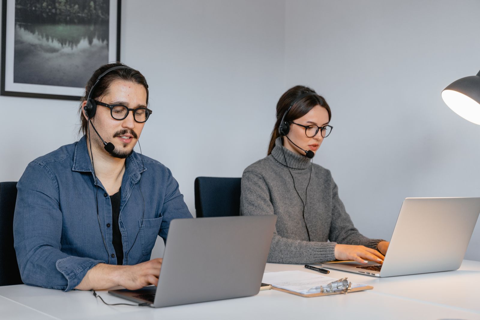 Two help desk engineers with headsets working at laptops