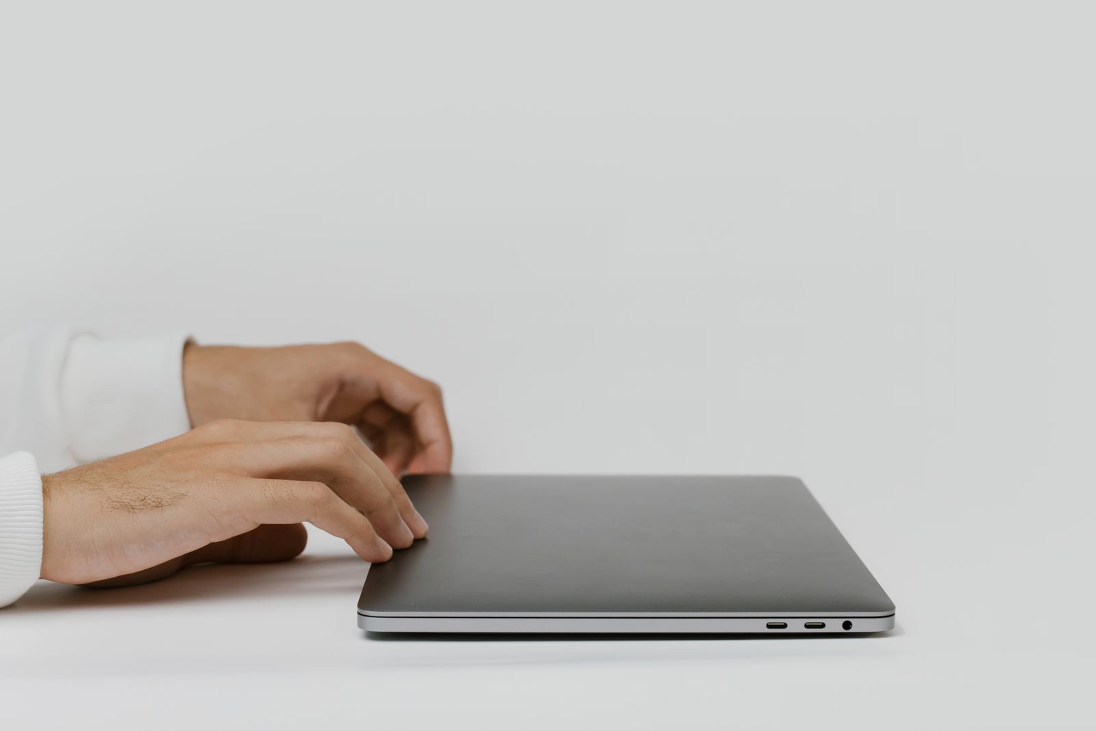 Hands about to open a closed laptop on a bare desk