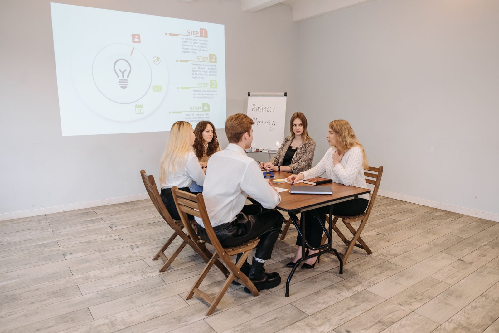 A small team in a meeting room watching a presentation on a screen