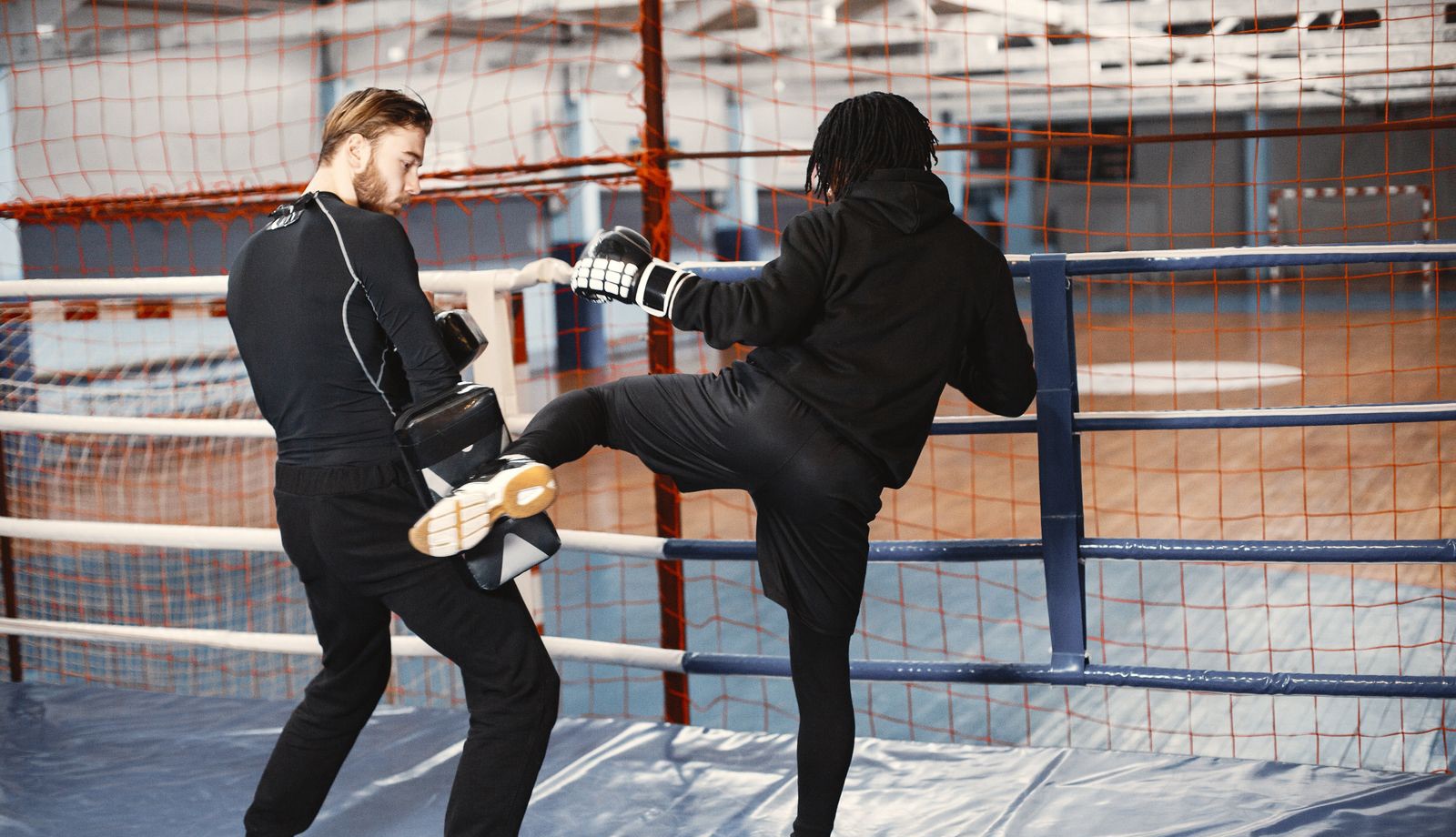 A kickboxer throws a lead-leg kick into a kick shield held by a coach inside a ring