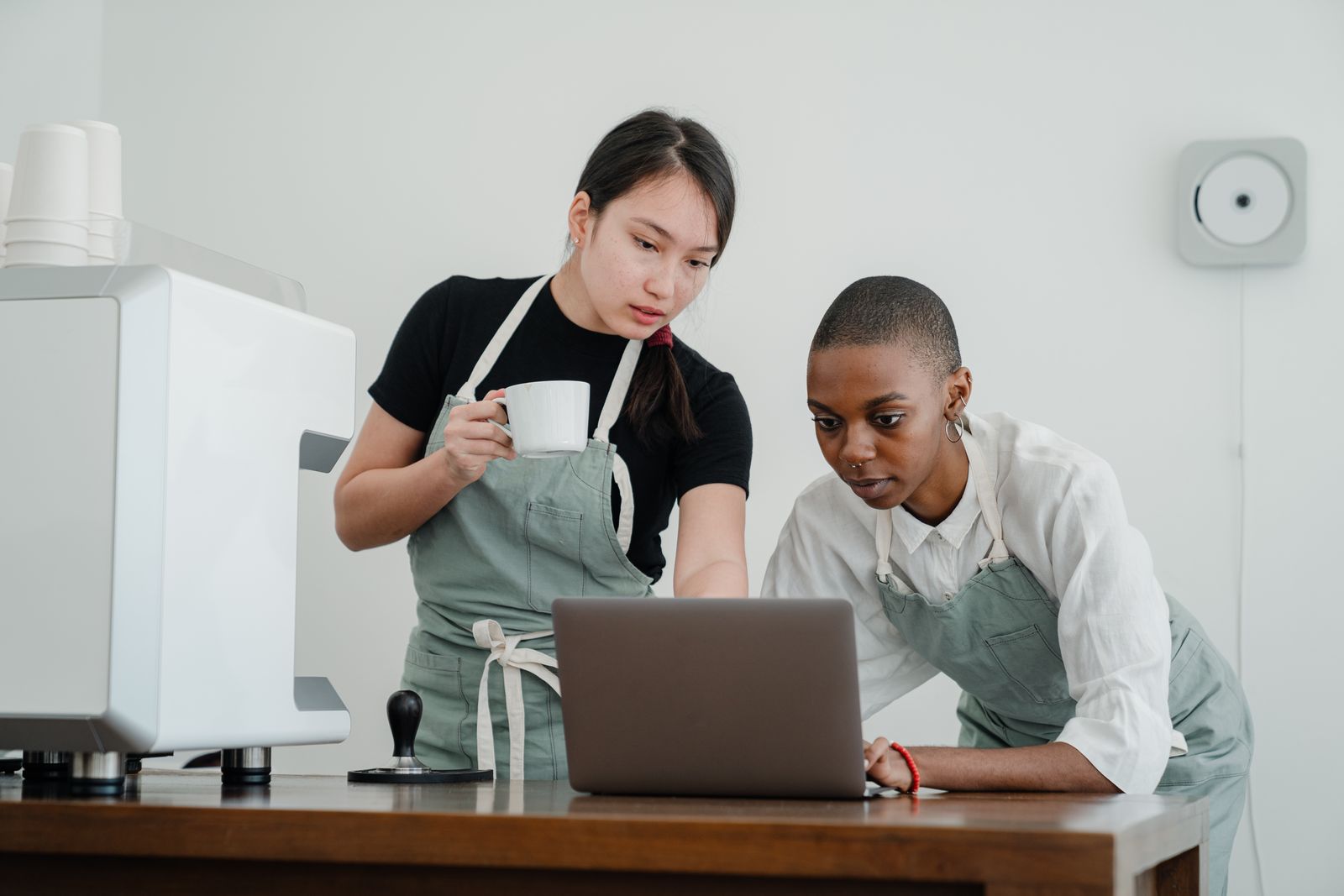 A cafe owner showing a new colleague the ordering system on a laptop