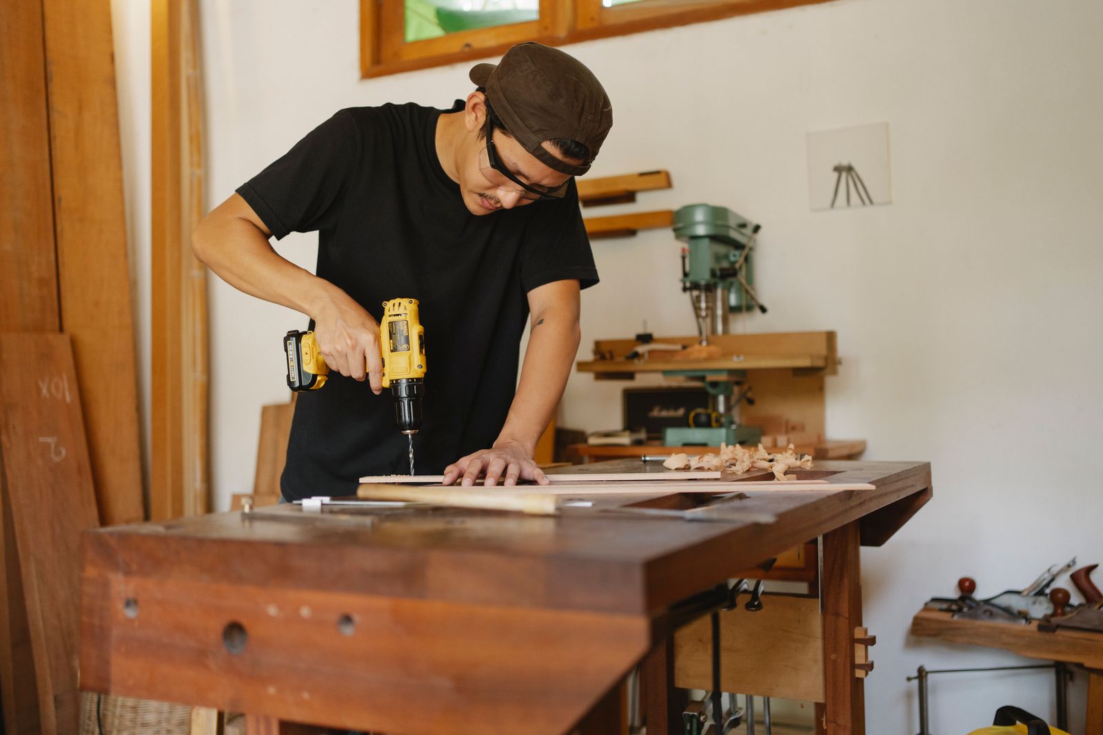 A joiner drilling a plank at a workbench in a small workshop