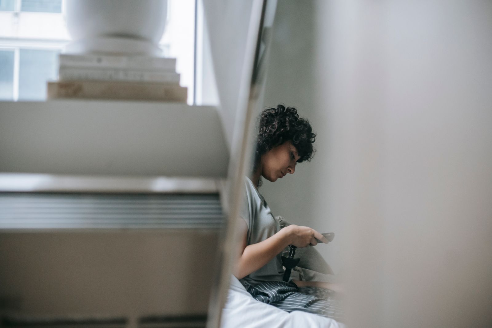 A person typing a message on a phone beside a pile of books, seen from the side