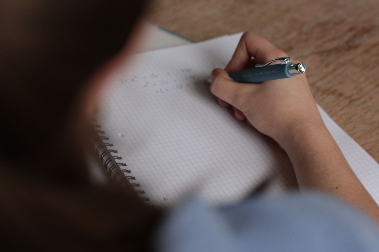 A student writing notes with a pen in a spiral notebook