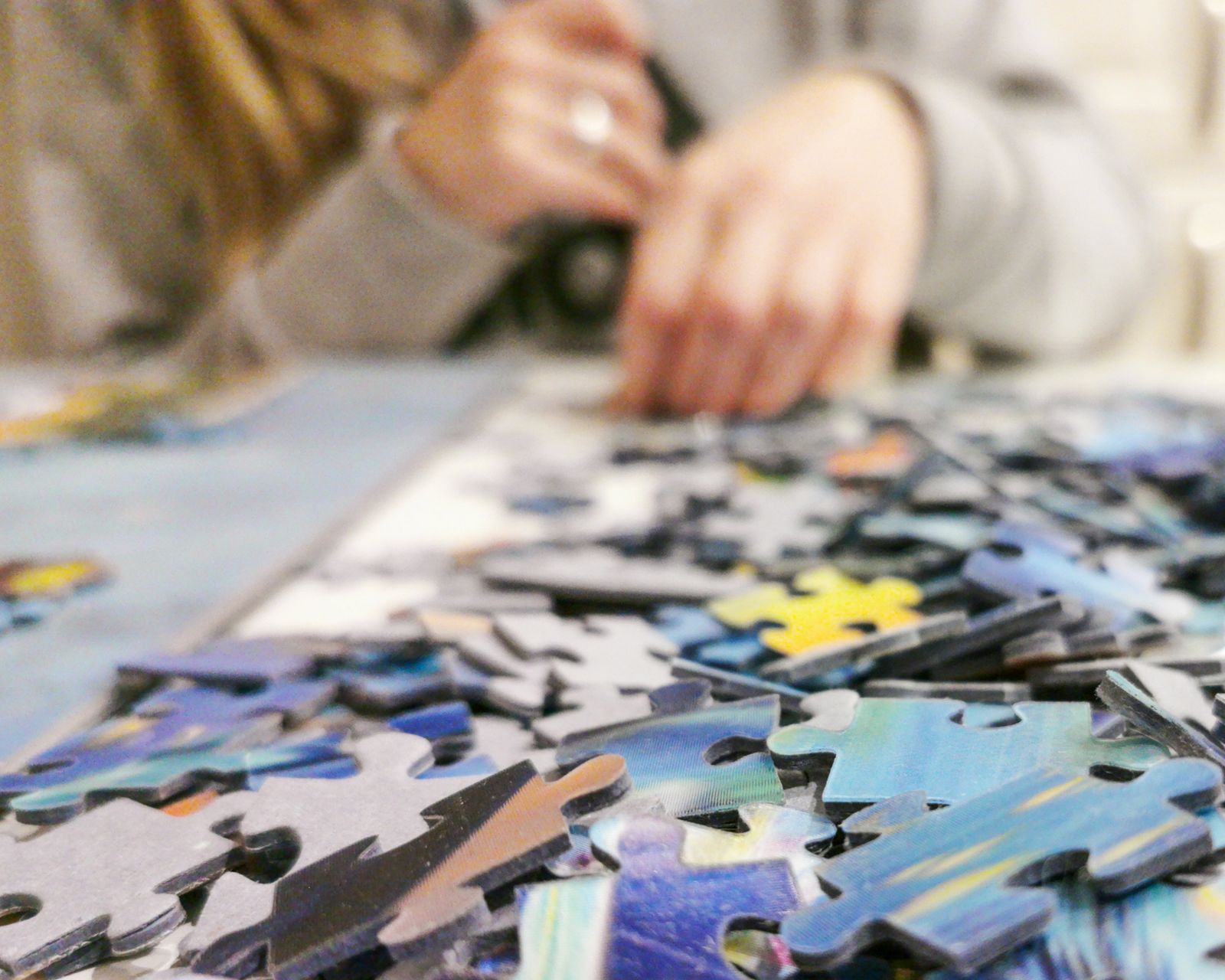 Hands fitting pieces into a colourful jigsaw puzzle on a table