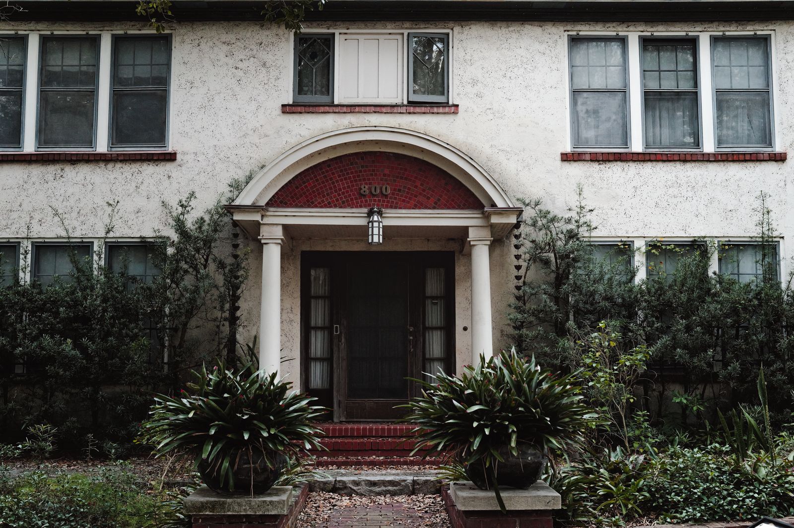 The front entrance of an old house with an arched porch, framed by climbing plants