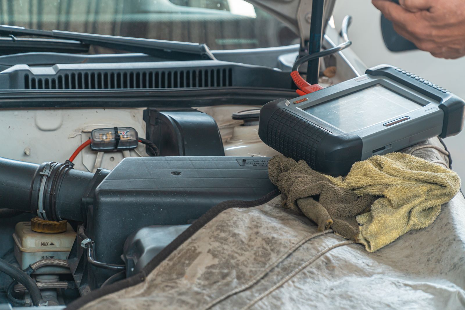 A diagnostic tablet resting on the engine of a car with the hood open