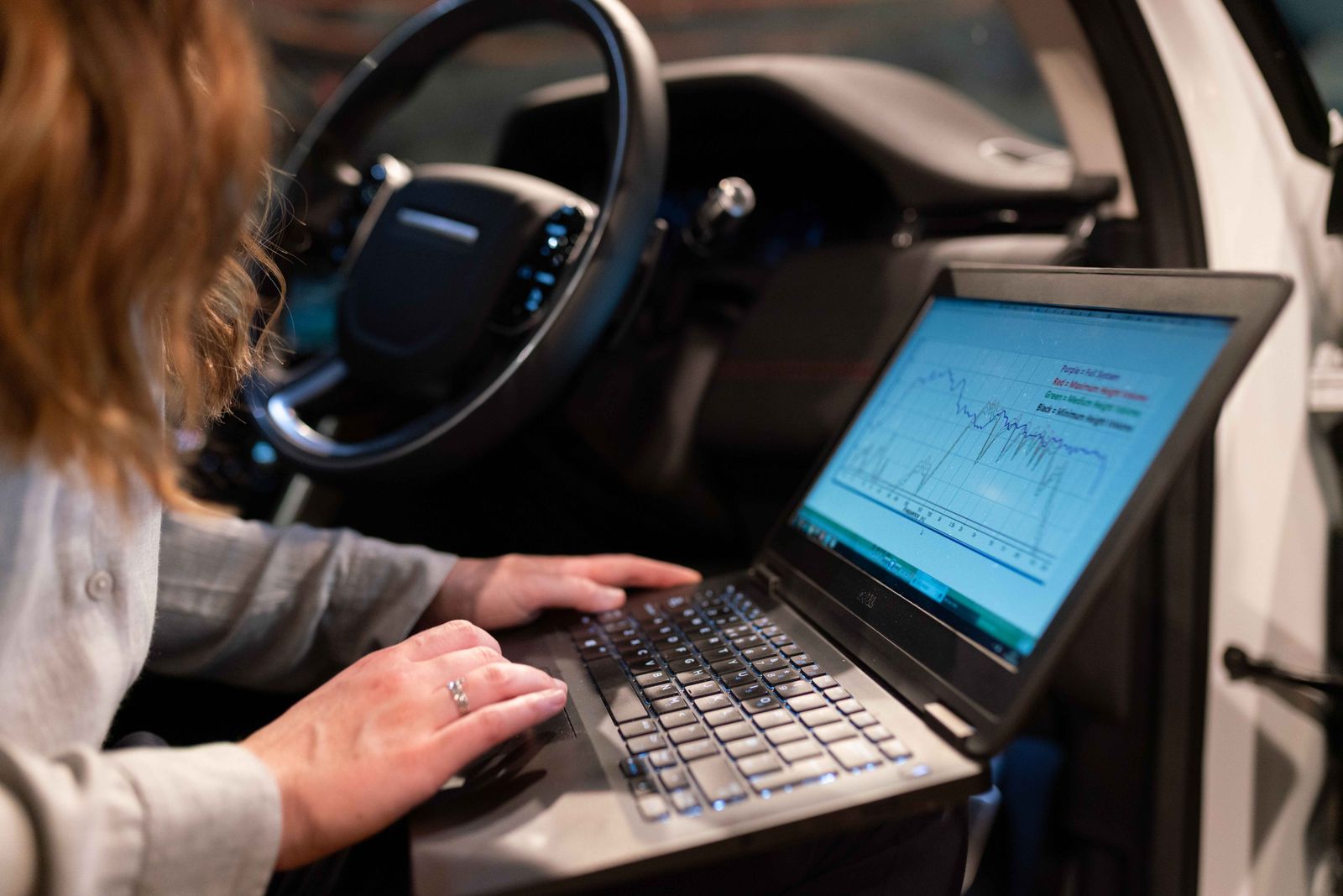 A technician reading vehicle data on a laptop from the driver's seat