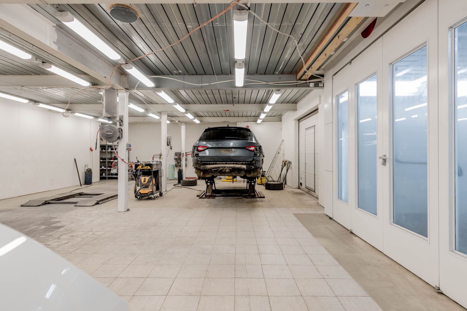 A long, tidy service hall with strip lights and a car waiting at the far end