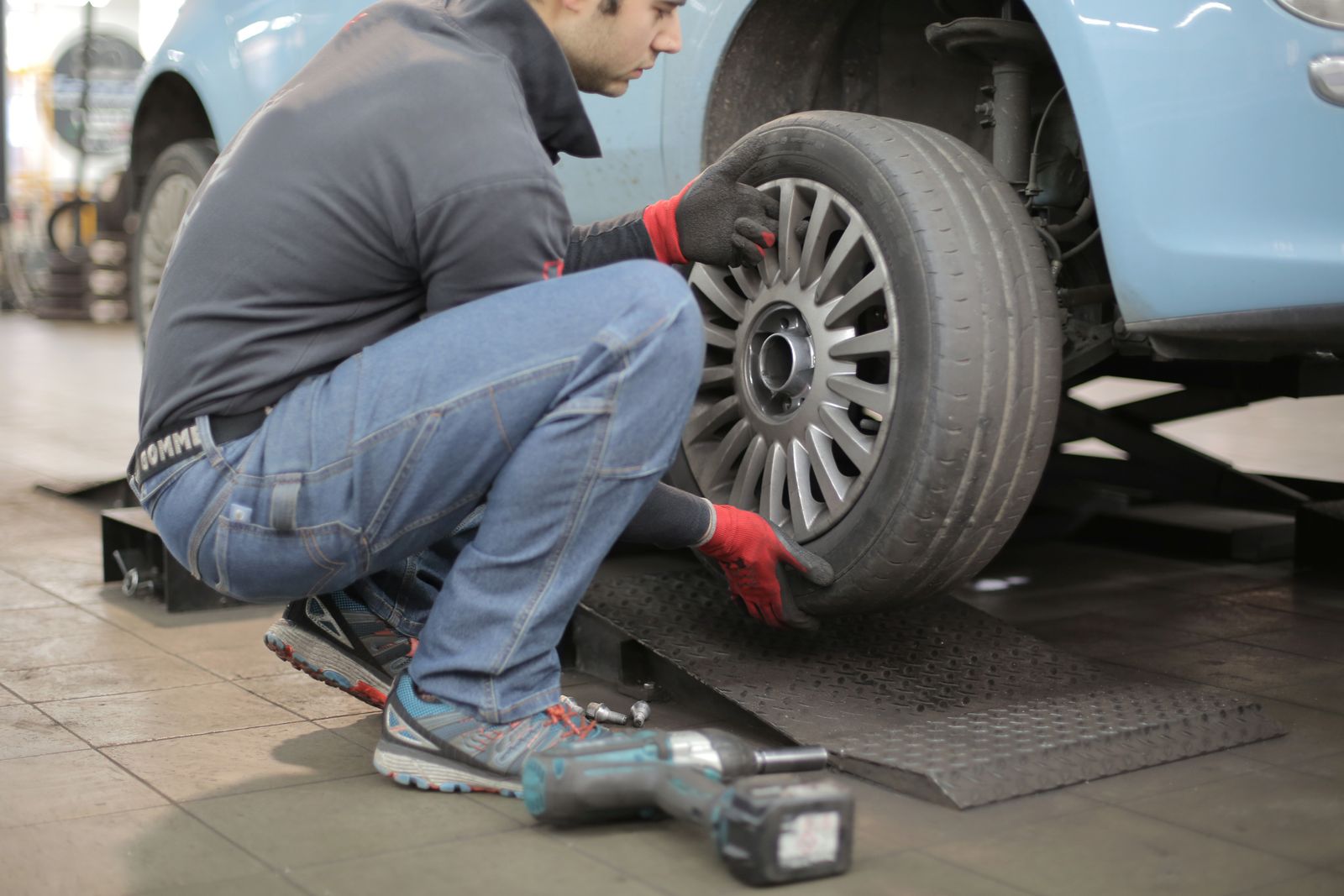 A technician kneeling to change a wheel on a raised car