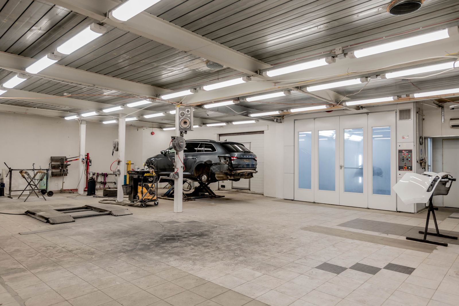 A bright workshop with a car on a lift and an empty bay in front