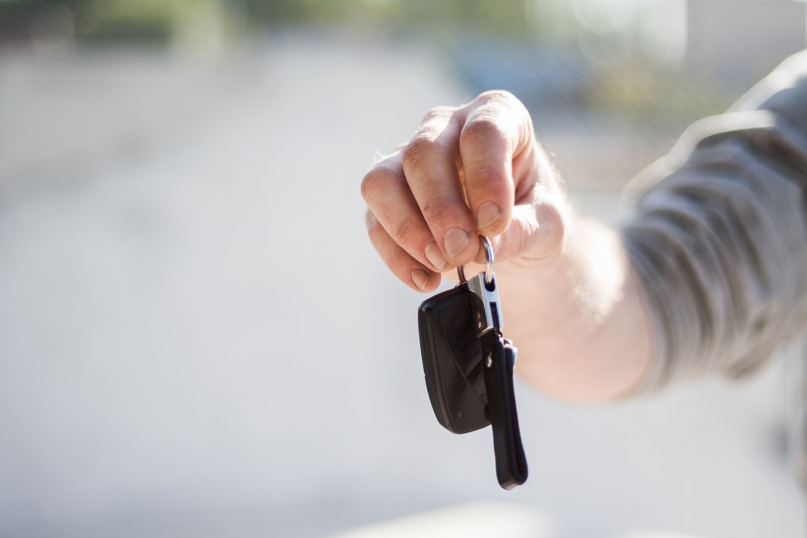A hand holding out a car key and its fob against a blurred grey background