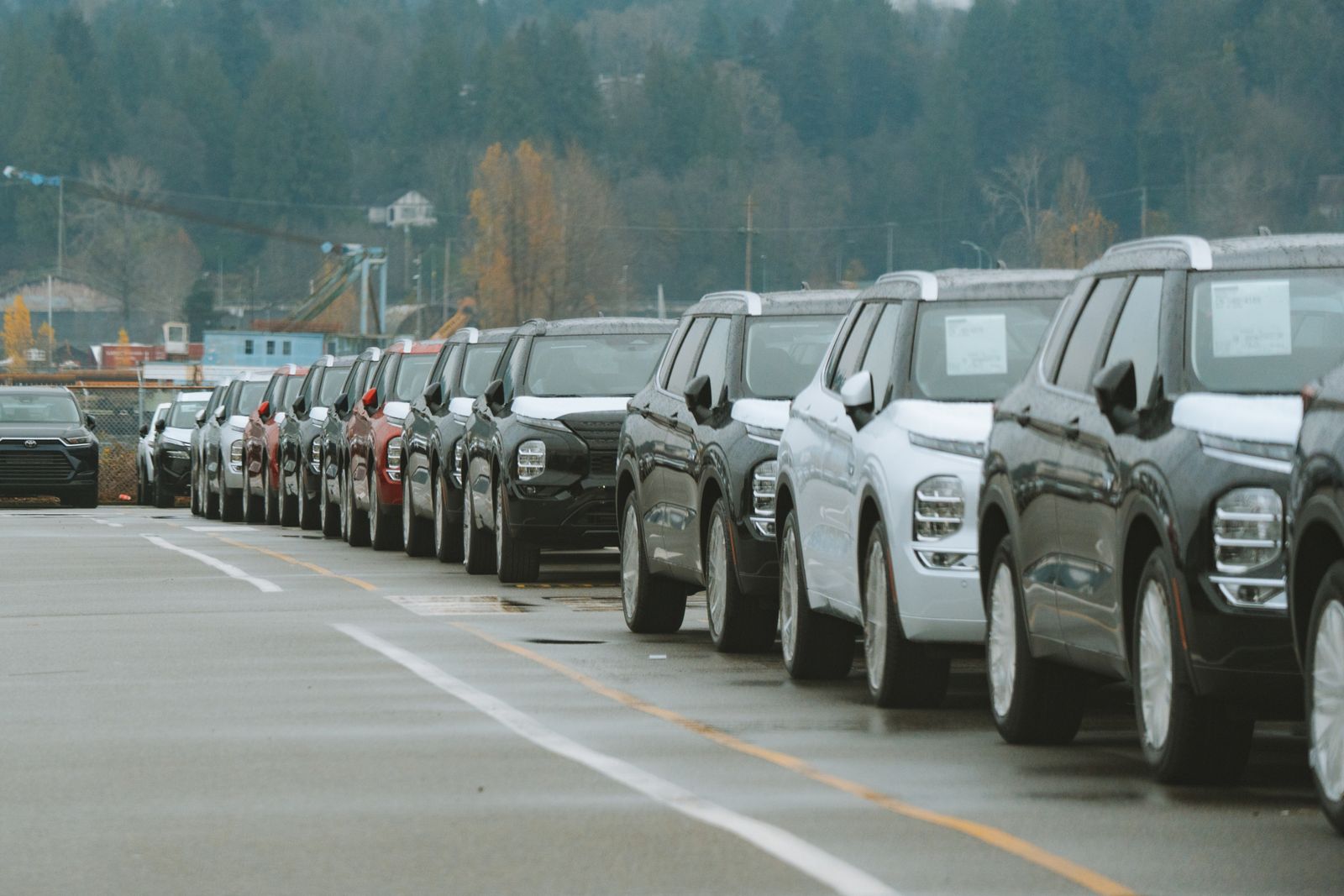 A row of SUVs parked on a dealer lot on a grey day, paper sheets on their windshields