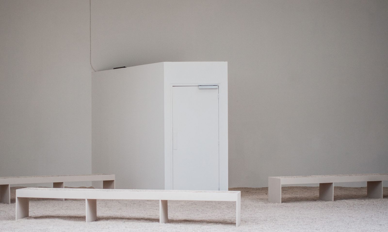 Empty white gallery room with low benches and a plinth